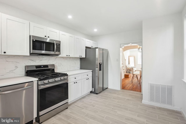 kitchen featuring arched walkways, stainless steel appliances, light countertops, visible vents, and backsplash