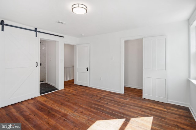 unfurnished bedroom with a barn door, visible vents, baseboards, and hardwood / wood-style floors