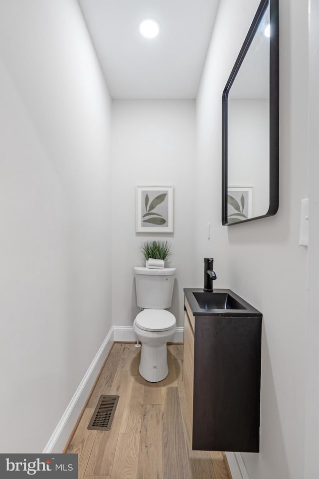 half bathroom featuring toilet, wood finished floors, vanity, visible vents, and baseboards