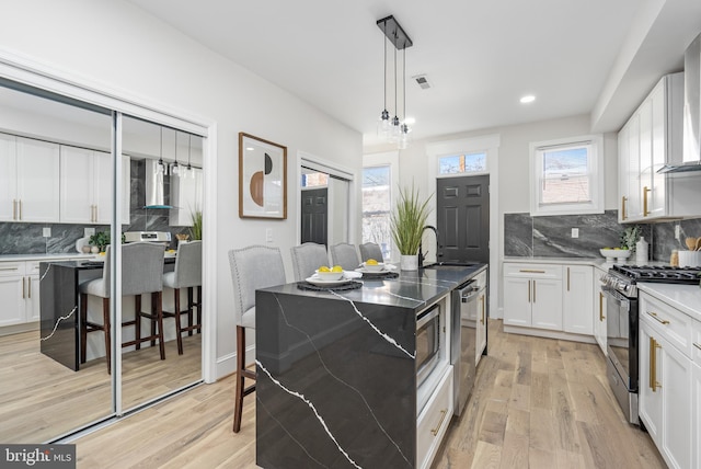 kitchen featuring light wood finished floors, wall chimney exhaust hood, white cabinetry, stainless steel dishwasher, and gas stove