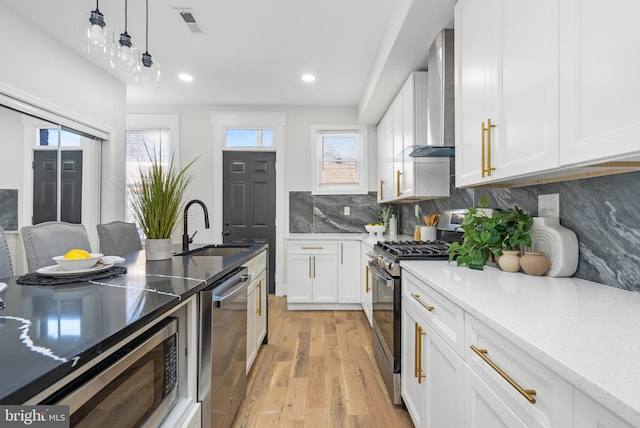 kitchen featuring tasteful backsplash, light wood-style floors, stainless steel appliances, wall chimney range hood, and a sink