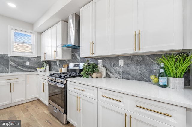 kitchen featuring light wood-style flooring, gas stove, white cabinetry, and wall chimney range hood