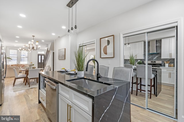 kitchen featuring a sink, light wood-style floors, dishwasher, wall chimney exhaust hood, and a center island with sink