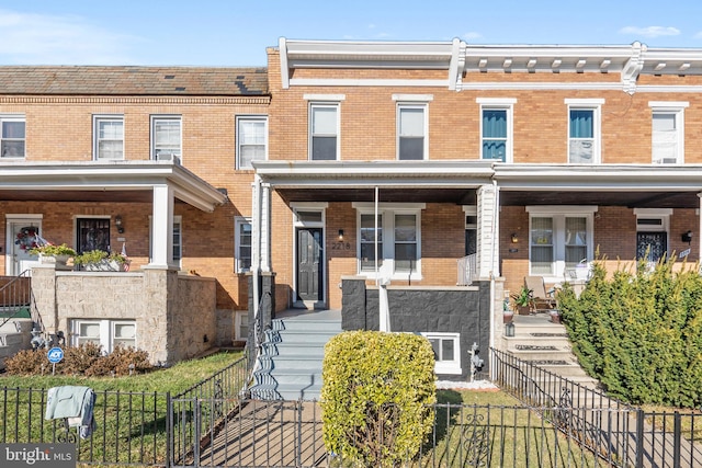 townhome / multi-family property with brick siding, a porch, and fence