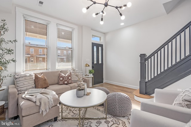 living room featuring a notable chandelier, wood finished floors, visible vents, baseboards, and stairway