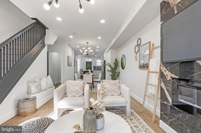 living area with a notable chandelier, recessed lighting, light wood-type flooring, baseboards, and stairs