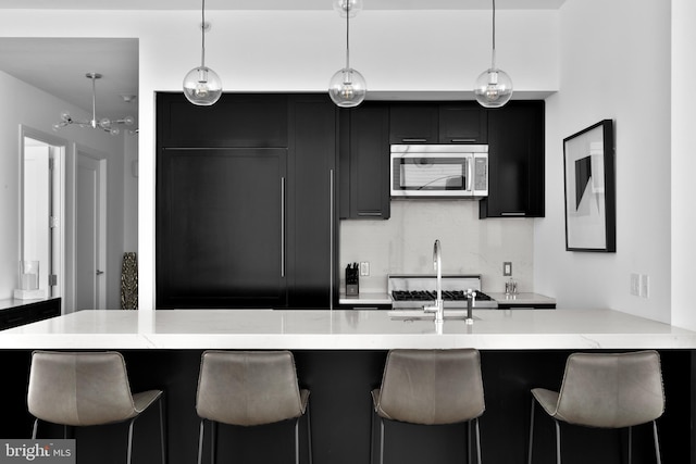 kitchen featuring pendant lighting, stainless steel microwave, a kitchen bar, and dark cabinets