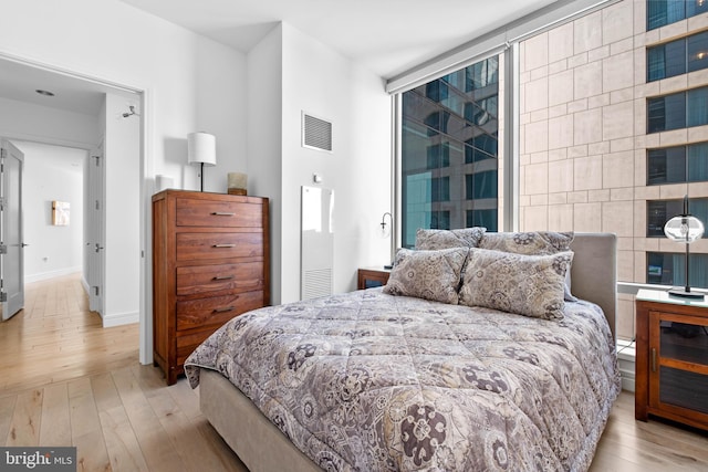 bedroom featuring expansive windows, light wood finished floors, and visible vents