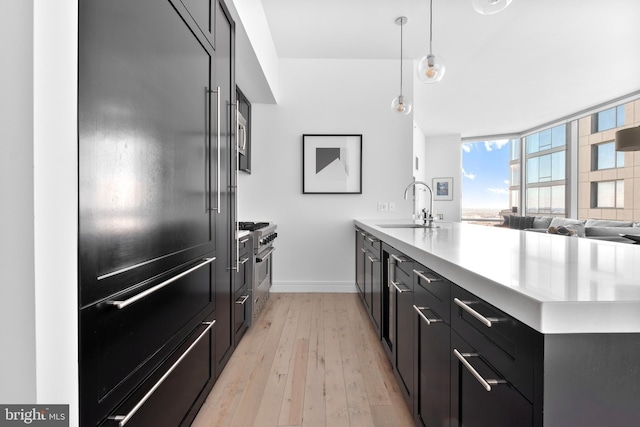 kitchen featuring premium appliances, light wood finished floors, light countertops, a sink, and a peninsula