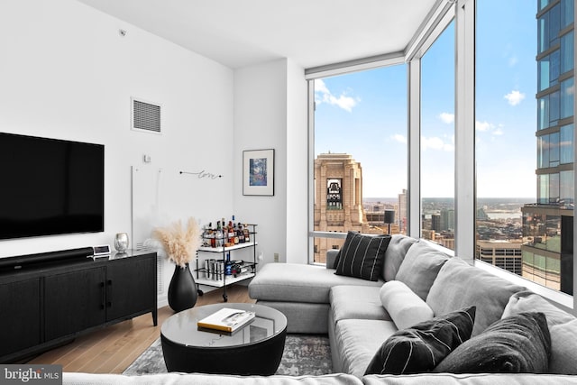 living room featuring a city view, light wood-type flooring, visible vents, and floor to ceiling windows