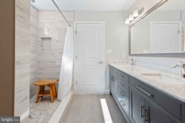 full bathroom with a sink, a tile shower, double vanity, and tile patterned flooring