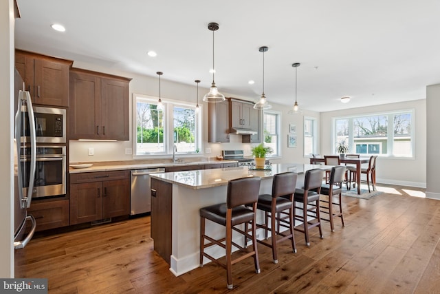 kitchen featuring a kitchen breakfast bar, a kitchen island, recessed lighting, stainless steel appliances, and wood-type flooring