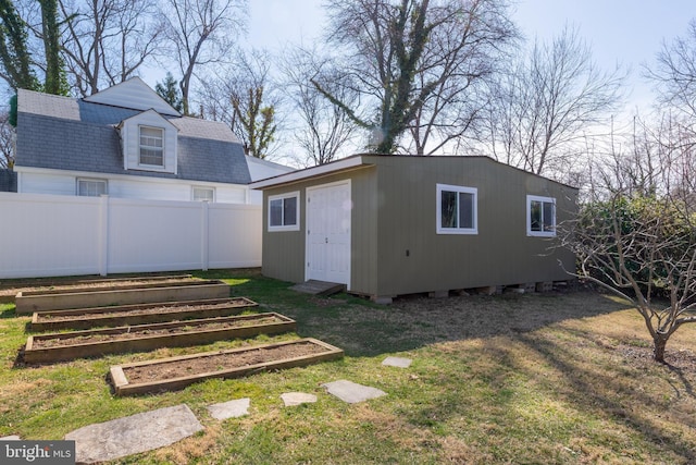 exterior space featuring an outbuilding, a lawn, fence, a vegetable garden, and a shingled roof