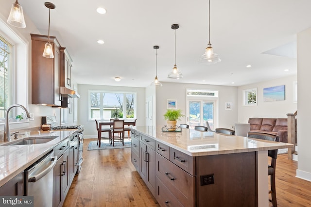 kitchen with a breakfast bar, light stone counters, light wood-style floors, stainless steel appliances, and a sink