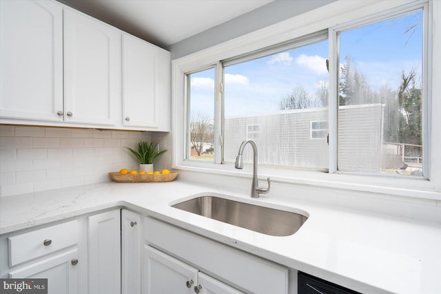 kitchen with tasteful backsplash, white cabinetry, light stone counters, and a sink