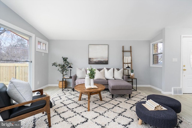 living area with light wood finished floors, visible vents, baseboards, and vaulted ceiling