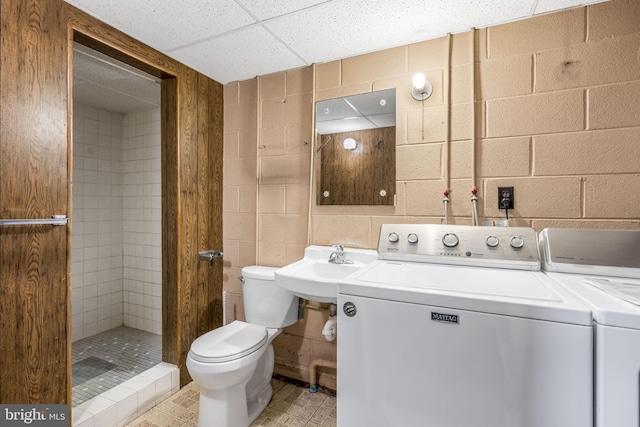 bathroom featuring concrete block wall, toilet, washing machine and clothes dryer, a shower stall, and a sink