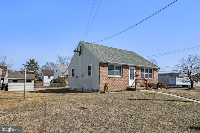 view of front facade with a shingled roof, brick siding, fence, and a front lawn