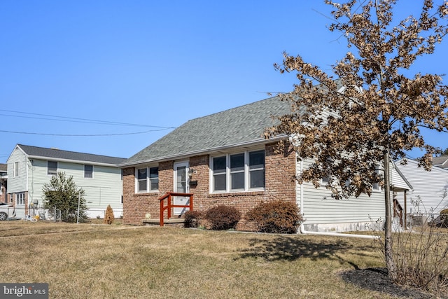 single story home featuring brick siding, roof with shingles, and a front yard