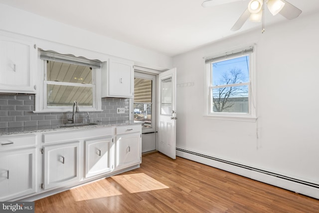 kitchen featuring a baseboard radiator, white cabinetry, a sink, and backsplash