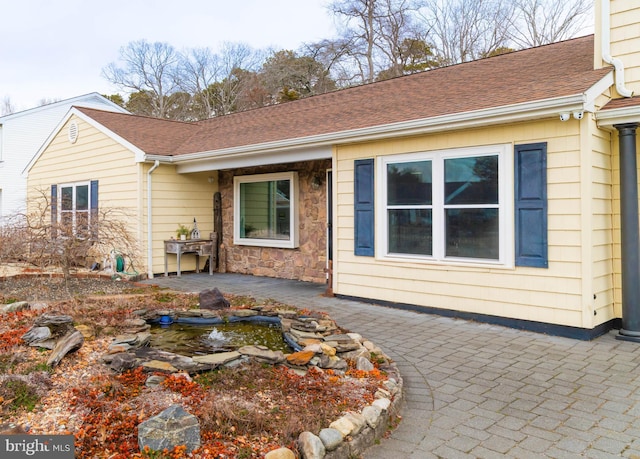 view of front of home with a shingled roof, stone siding, and a patio