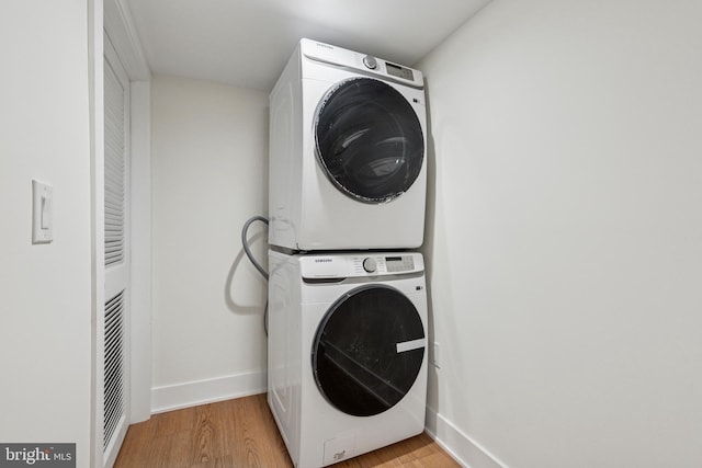 washroom featuring light wood finished floors, baseboards, laundry area, and stacked washer / drying machine