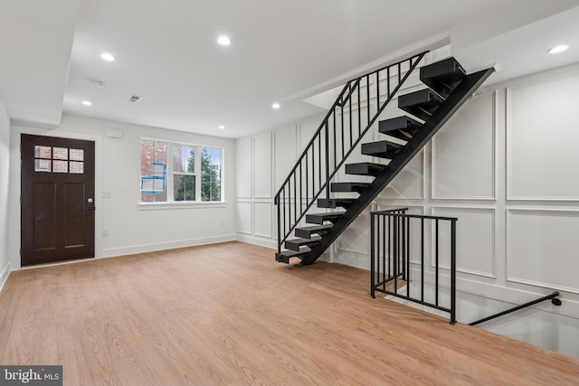 entryway with visible vents, stairway, wood finished floors, a decorative wall, and recessed lighting