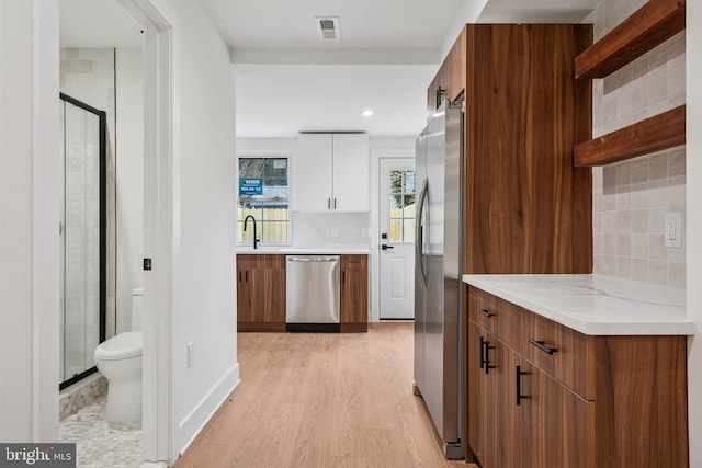 kitchen featuring visible vents, white cabinets, appliances with stainless steel finishes, light wood-type flooring, and decorative backsplash