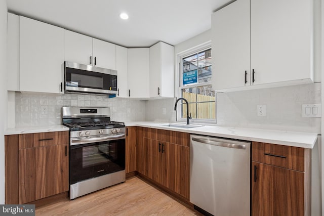 kitchen with light wood finished floors, appliances with stainless steel finishes, light countertops, and a sink