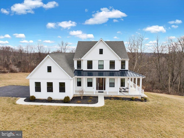 modern farmhouse featuring roof with shingles, covered porch, a front yard, a standing seam roof, and metal roof