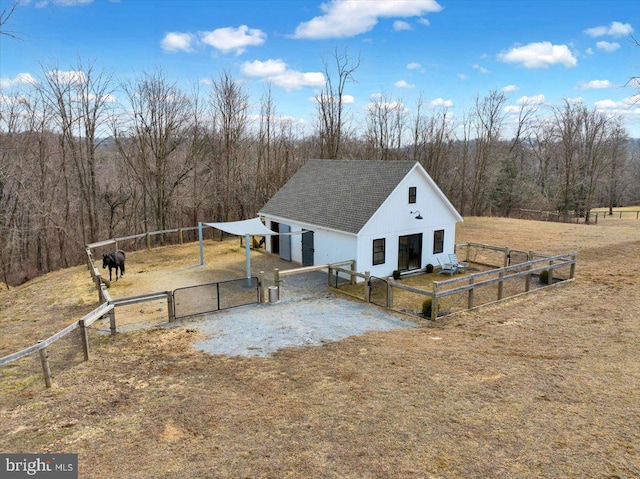 view of front of home with roof with shingles, gravel driveway, a gate, an outdoor structure, and a wooded view