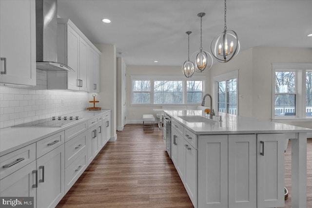 kitchen featuring dark wood finished floors, light countertops, white cabinets, a sink, and wall chimney range hood