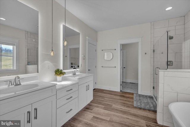 full bathroom featuring double vanity, a stall shower, a sink, wood finished floors, and a freestanding tub