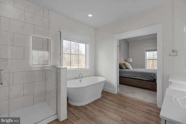 ensuite bathroom featuring a wealth of natural light, a shower stall, a freestanding bath, and wood finished floors