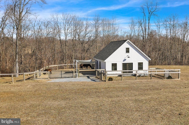 exterior space featuring an outbuilding, a gate, roof with shingles, and a wooded view