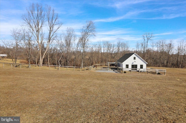 view of yard with a rural view, an outdoor structure, a wooded view, and fence