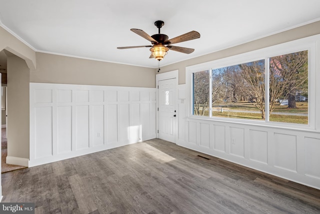 unfurnished room featuring a decorative wall, crown molding, a ceiling fan, and wood finished floors