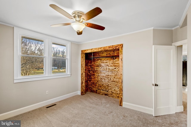 unfurnished bedroom featuring visible vents, crown molding, baseboards, carpet floors, and a ceiling fan