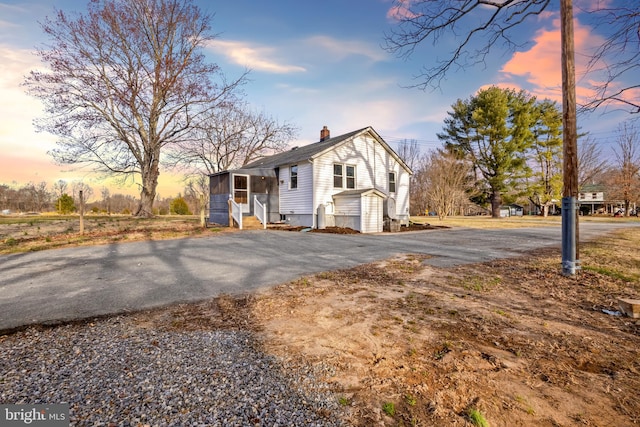 view of front of home featuring entry steps, driveway, a sunroom, and a chimney