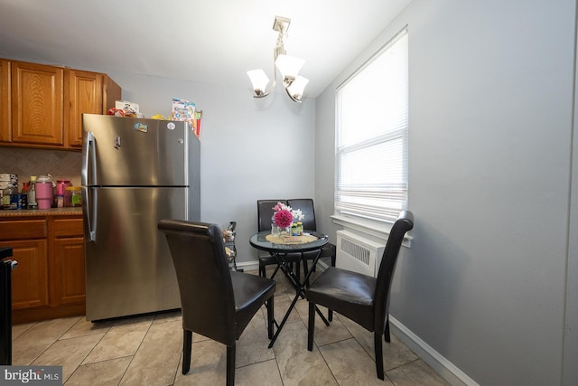 dining room featuring baseboards, light tile patterned floors, radiator heating unit, and a notable chandelier