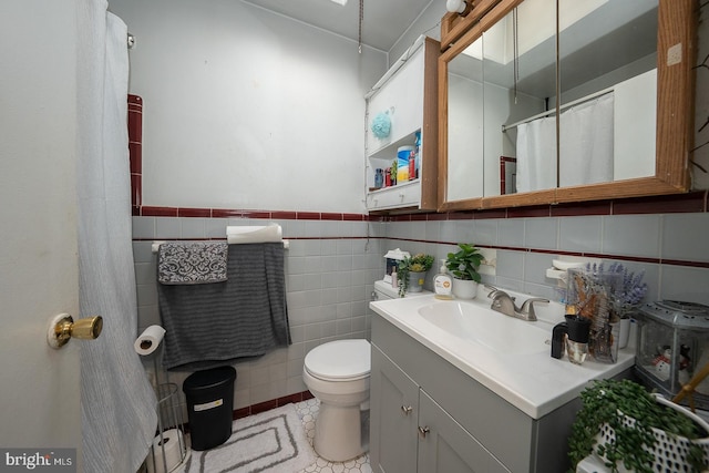 bathroom with toilet, a wainscoted wall, vanity, tile walls, and tile patterned floors