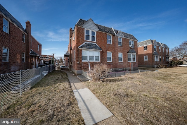 view of front of home with brick siding, a chimney, a front yard, and fence