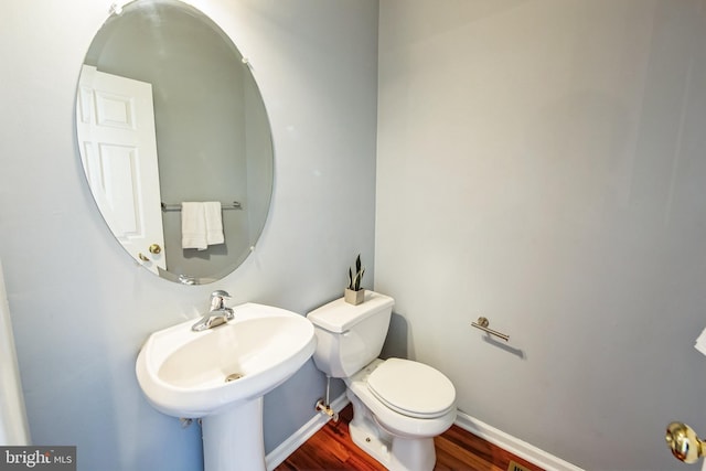 half bathroom featuring a sink, baseboards, toilet, and wood finished floors