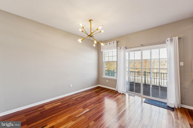 empty room featuring a notable chandelier, wood finished floors, and baseboards