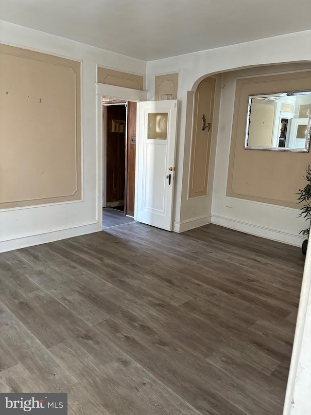 spare room featuring dark wood-style floors, baseboards, and arched walkways