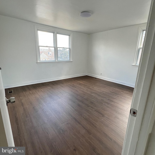 unfurnished room featuring dark wood-type flooring, visible vents, and baseboards