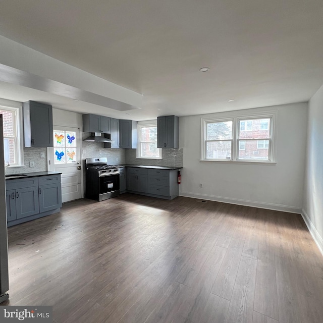 kitchen featuring stainless steel gas stove, tasteful backsplash, dark wood-style floors, extractor fan, and gray cabinets