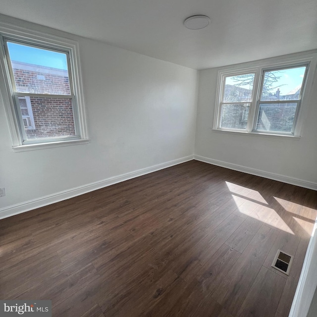 unfurnished room featuring dark wood-style floors, visible vents, and baseboards