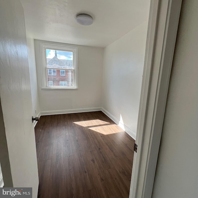 spare room featuring dark wood-type flooring and baseboards