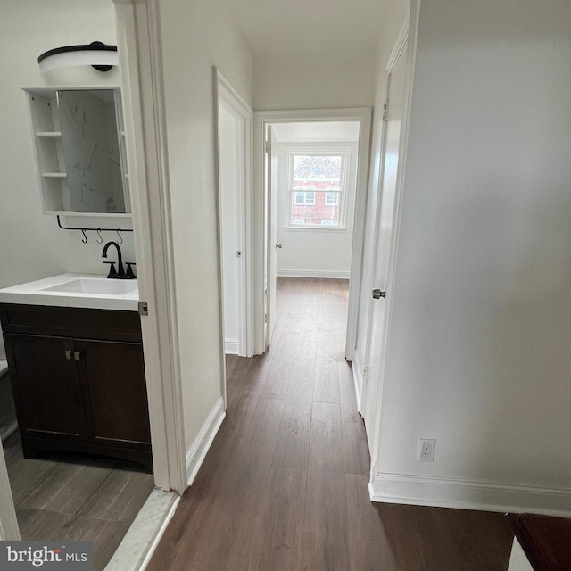 hallway with dark wood-type flooring, a sink, and baseboards